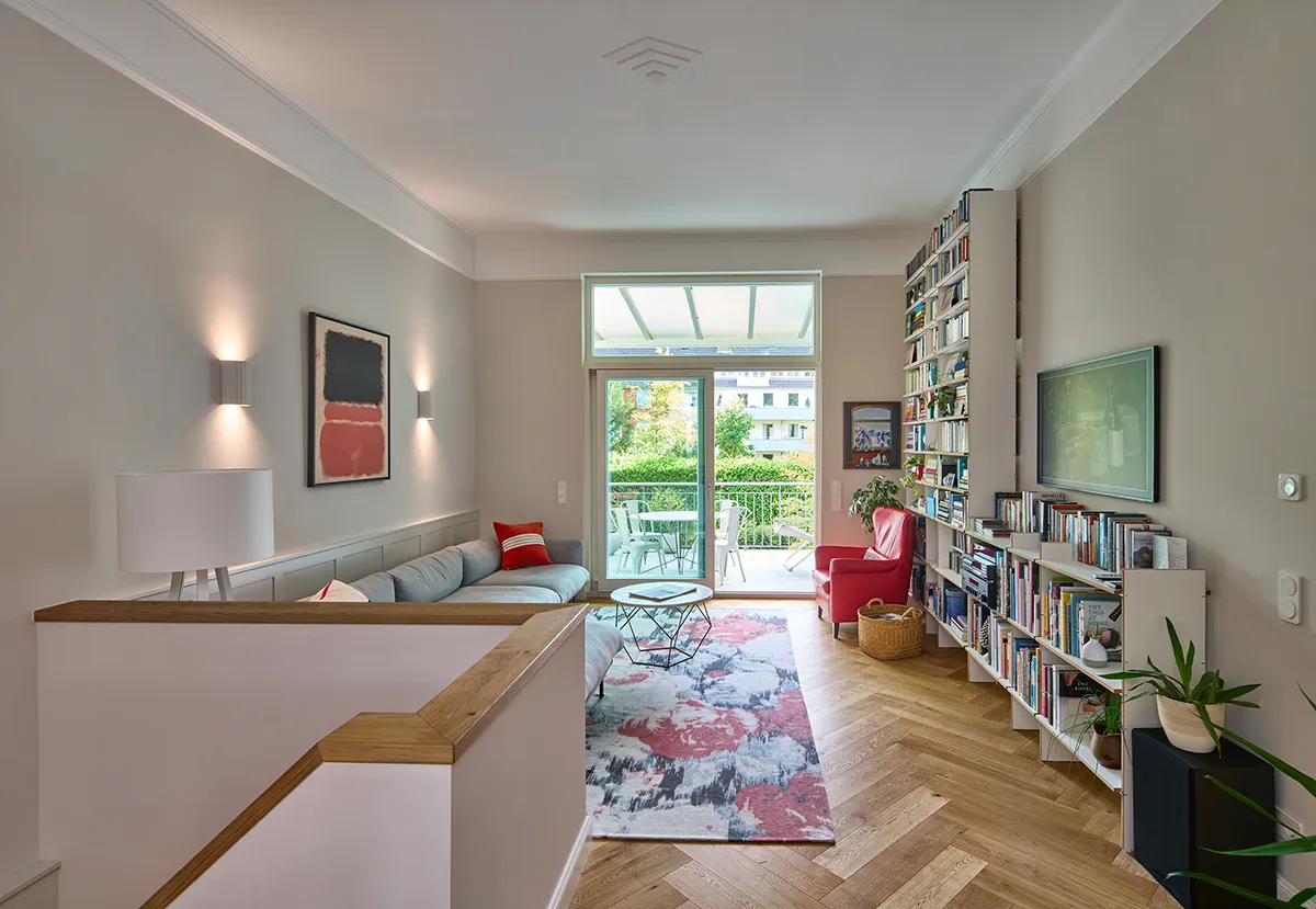 Wohnraum einer modernisierten Maisonettewohnung mit offener Galerie, Eichenparkett im Fischgrätmuster, integrierter Bücherwand und Zugang zur verglasten Terrasse.